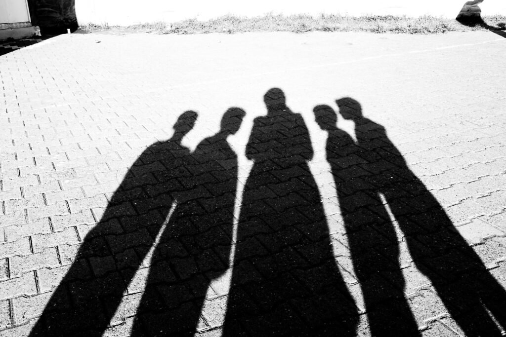 Silhouettes of people casting shadows on a textured stone pavement in bright daylight.