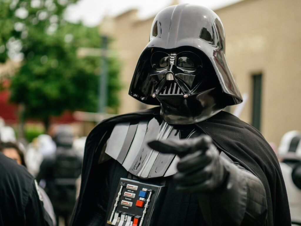 Darth Vader cosplayer pointing in an outdoor setting, showcasing detailed costume and helmet.