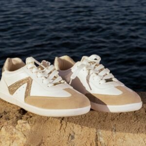 Trendy beige and white sneakers placed on a stone surface by the water, perfect for lifestyle and fashion themes.